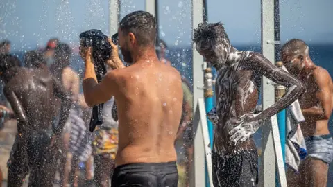 Europa Press via Getty Image Migrants use outdoor showers at a beach encampment in Ceuta, Spain, 25 August 2026