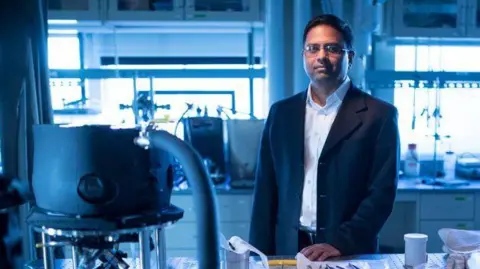 MIT Prof Varanasi standing in a laboratory surrounded by lab equipment