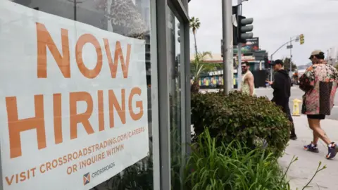 A 'Now Hiring' sign is displayed outside a resale clothing shop 