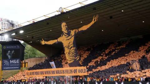 BBC A large banner is on show in the South Bank at the Wolves ground. It is gold and black and Jota is captured celebrating with his arms outstretched with the words "We'll remember you when you walk in fields of gold" at the bottom.