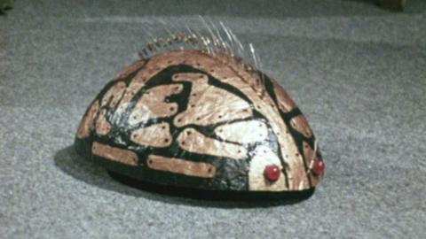 Rounded metal, robotic pet with bronze pattern on curved back, metal spikes and red eyes. 