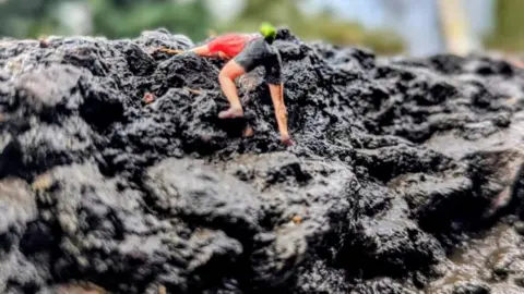 Miniature mountain climber figures placed inside a pothole, pictured as though they are climbing a mountain