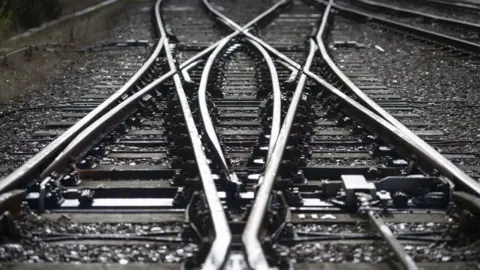 A junction with two train tracks intersecting on a grey day. 