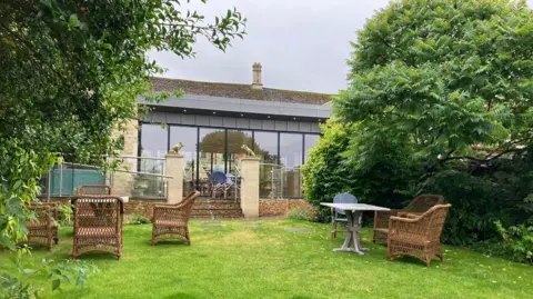 Hotel garden with lawn and building made from cotswold stone and glass qhidqhieqiqxtinv