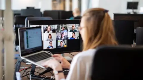 Getty Images Rear view of a woman sitting in an office on a video call with team members