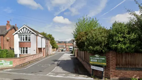 A streetview image of a private road leading to industrial buildings. Signs directing visitors to a pet and garden store can be seen on either side of the road.