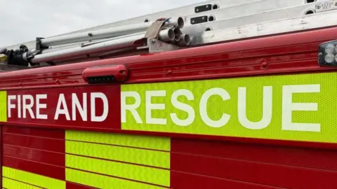 The side of a fire engine in red and green/yellow, with "Fire and Rescue" written on the side