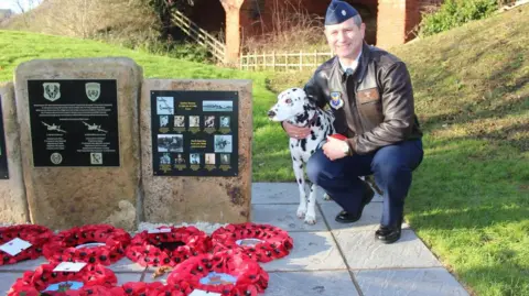 South Kesteven District Council Lt Col Chris Nastal pictured at the memorial with a Dalmatian dog with wreaths in the foreground.

