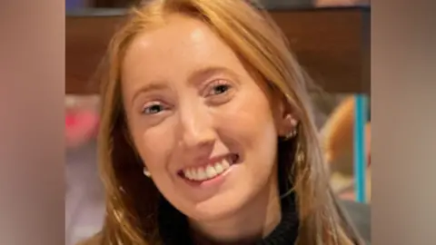Close up of Chloe Moffat, who has long red hair, smiling at a camera.
