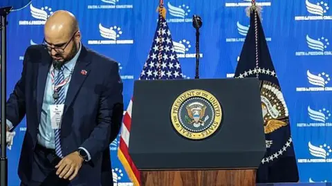 White House teleprompter operator Gabriel Perez sets up a teleprompter before US President Donald Trump speaks at the Faith & Freedom Coalition's 2026 Policy Conference at the Washington Hilton in June.