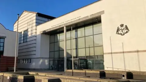 The Isle of Man Court of Justice building, which is a large white building with a glass front and the government crest on the wall.