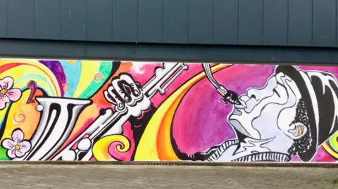 Viva Slough A mural showing a man playing a saxophone. It includes bright colours such as pink, orange and yellow.