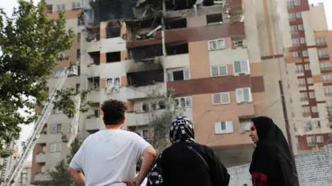 People look at a damaged building in the aftermath of Israeli strikes, in Tehran, Iran.