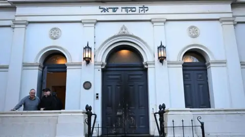 Fire marks on the blue door of the East Melbourne Hebrew Congregation in Melbourne, with two men to the left in front of an open window
