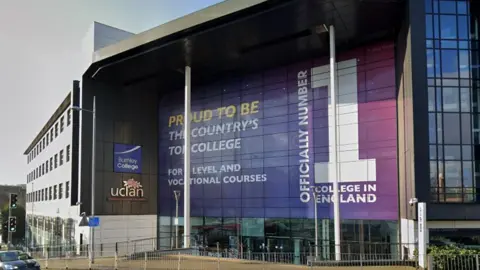 Street view image of Burnley College, a huge building with an imposing front entrance with white steel pillars and a large glass-fronted area with a huge purple sign saying 'Official no 1 college in England'