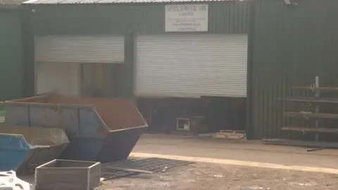 Exterior view of Weldrite UK factory building with roller doors and industrial skips outside.