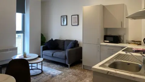 A kitchen sink and living area with a floor-to-ceiling window at the back of the room.