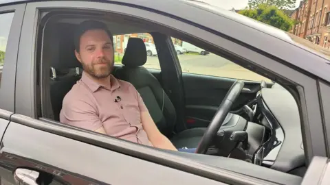 Jason Keley sitting in the driver's seat of his car looking out of the window