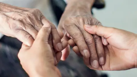 Getty Images Carer holding elderly person's hands