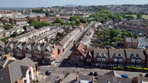 Rows of terraced houses stand on either side of streets with a glimpse of the sea behind them in the distance.