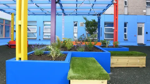 Your RWTC The colourful garden at the hospital. Planters are painted blue as are the walls. A hard floor has been put down with seating and new windows.