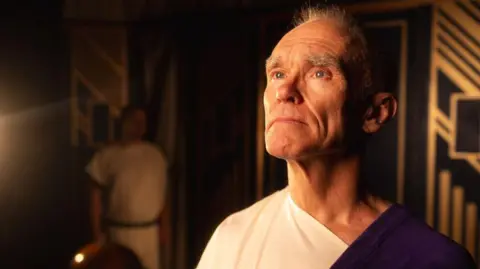 Derby Shakespeare Theatre Company Image of Ian Currie as Julius Caesar on stage. He is wearing a toga.