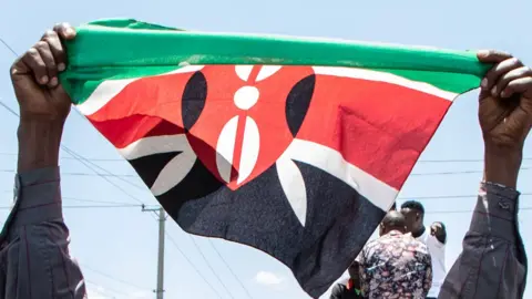 Two fists are folding up a Kenyan flag.