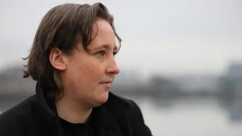 Indelible Telly/BBC A side on view of Mhairi Black - she has short brown hair, is outdoors and is wearing a black coat as she looks to the right