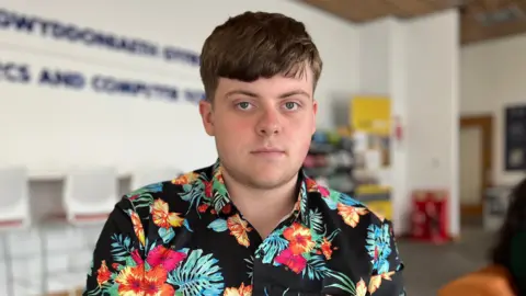 A young man in a pink shirt looks at the camera