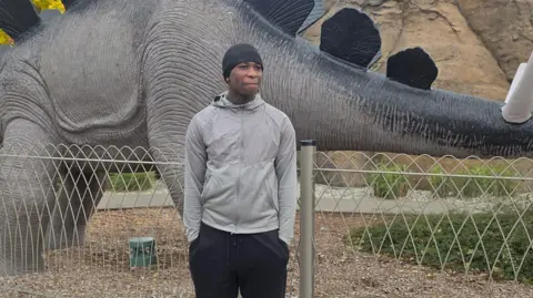 Family handout Eghosa Ogbebor pictured standing in front of a dinosaur sculpture