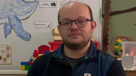Phil Massey. He is bald, wearing glasses and a blue half-zip fleece.
