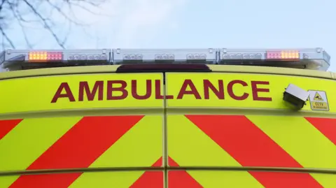 A stock image of the back of an ambulance with its lights on.