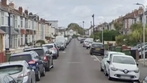 Hartley Road is a suburban street with terraced houses on either side, and cars parked along the curb on both sides.