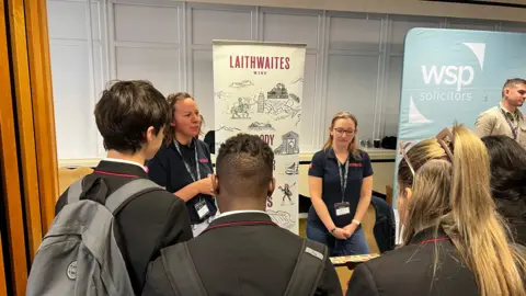 Four students grouped around a stall with two reps in navy tops talk to them