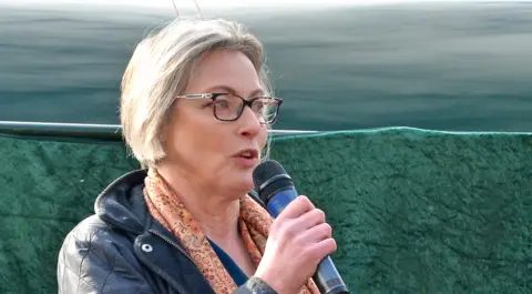 Watercress Line Rebecca Dalley talks into a microphone as she stands in front of a steam locomotive