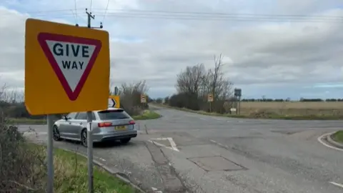 General image of the Wheatsheaf crossroads. There is a Give Way sign and a car waiting at the crossing