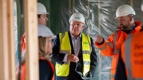 Wrekin Housing Group Three men and a woman in hard hats and high-vis jackets on a building site discussing things