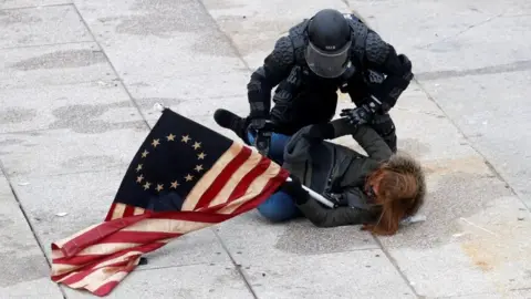 Pro-Trump protester holding vintage US flag lies on ground with police officer trying to detain them