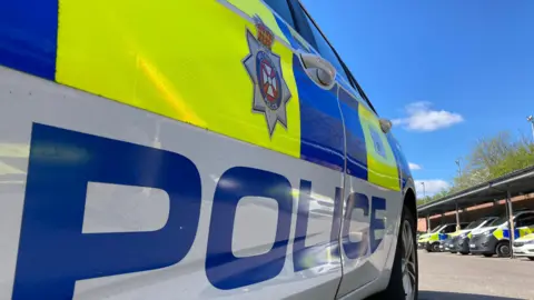 The door of a police car with the word "police" written prominently on the side and a Wiltshire Police badge above.