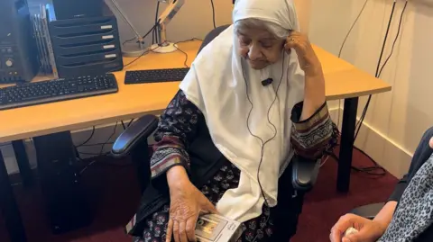 Woman sat successful  beforehand   of a table  listening to a portable cassette recorder