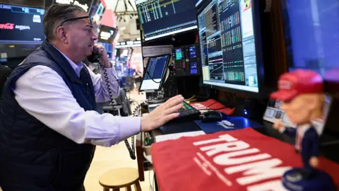 A trader at the New York Stock Exchange talks on the phone while gesturing in front of screens with stock market numbers on, and a toy doll of Donald Trump on the desk in front of him, in New York on Wednesday.