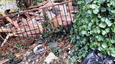 Basildon Council Fly tipped rubbish on the ground outside. There is a large bin bag which has been tied up as well as a large pile of broken planks of wood. 