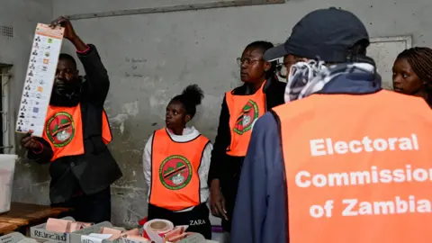 An election official displays a ballot paper as observers look on during the counting of votes after the polls closed at a polling station in Lusaka, Zambia