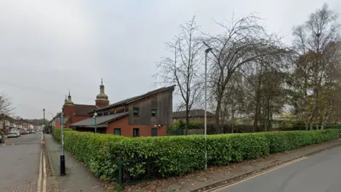 Google A hedge runs along the side of both streets and meets on a corner from where the photo has been taken. A red-bricked and wooden-clad building can be seen on the left of the image, behind the hedge and next to the gold-looking spires of the Ukrainian church.