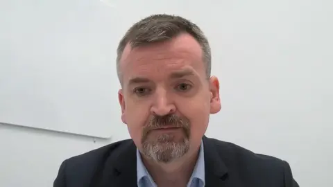 Martin Sutherland, the former CEO of the trust. He has short brown greying hair, a beard and a moustache. 