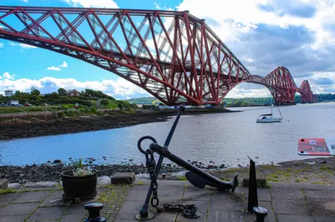 Samantha Christie A view from a pier looking up a large red bridge, stretching for miles into the distance. 