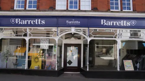 John Fairhall/BBC The frontage of an independent department store. It is predominantly made up of glass windows but along the top of the entrance to the shop is a blue and white banner of branding which reads Barretts, then, Barretts of Woodbridge, and then Barretts again. There are displays in the windows.