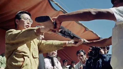 AFP Peruvian President Alberto Fujimori hands a weapon to a peasant in Huancayo on June 23, 1991