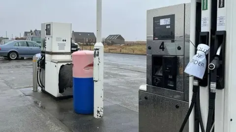 BBC A filling station in Uist on a wet day, There is a row of pumps and a paper notice wrapped around one that says "out of order".