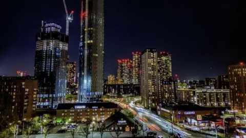 A number of high-rise buildings - making up Manchester's skyline - are in view. On the left-hand side, a crane is positioned on top of a building which is currently under construction. 